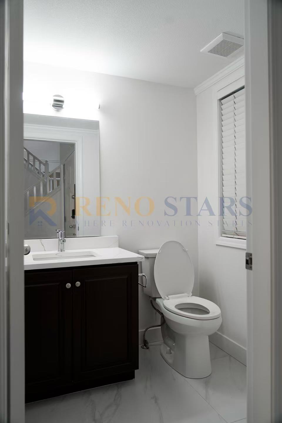 Modern bathroom featuring a dark wood vanity, white sink, and a toilet in a bright space.